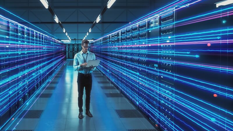 Man staat met een laptop in zijn hand in een ruimte met allemaal servers