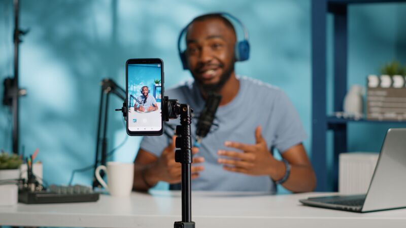 Een telefoon neemt een content creator op die achter een bureau iets aan het vertellen is