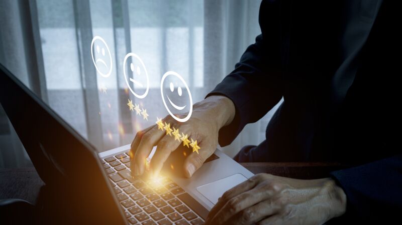 Een man typt op een laptop. Er is een hologram boven het toetsenbord van een review systeem met sterren en emojjis