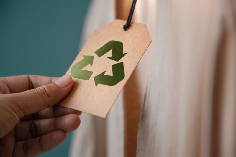 Een hand houd een kaartje met een recycle teken vast