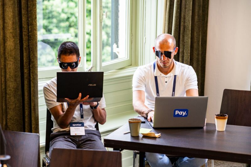 Twee mannen zitten achter een laptop met brillen op hun hoofd die een beperking nabootsen